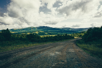 Dramatic green landscape with dirt road in towards mountains under cloudy sky.