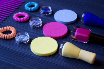 Colorful and bright cosmetics. Beauty care tools. Beauty salon. Girl's paradise.  Nail polishes, sequins, pink hair bands and comb on a dark blue wooden desk. Bright still life of beauty instruments.