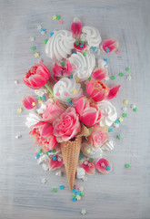 Flatlay waffle sweet ice cream cone with pink tulips and roses blossom flowers over white wood background, top view. Spring or summer mood concept.