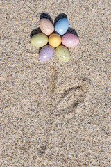 Flower shape made of colorful Easter eggs on the beach in sunny day. Easter concept.