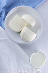 Cheese, cheese on a white plate, a glass of yogurt, minimalism, top view, copy space, dairy products on a white napkin, blue cloth, cheese pattern, French breakfast, white cheese on a white background