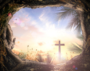 Palm Sunday concept: Silhouette cross and empty tombstone with palm leaves over meadow sunset background	