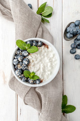 Cottage cheese with fresh blueberries and mint leaves on a white board background..
