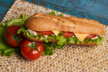 Fresh submarine sandwich with chicken fillet, cheese, fresh tomatoes, lettuce, cucumbers and onions on wooden background