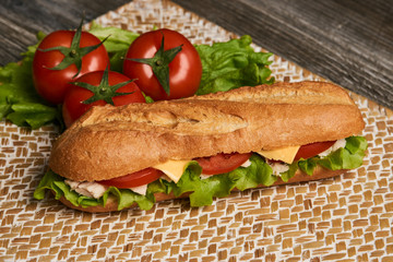 Fresh submarine sandwich with chicken fillet, cheese, fresh tomatoes, lettuce, cucumbers and onions on wooden background