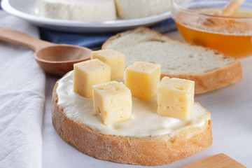 Cheese on a white plate, a glass of yogurt, a sandwich with soft cheese, minimalism, top view, copy space, a piece of bread with hard cheese, blue cloth, French breakfast, white cheese on a white back