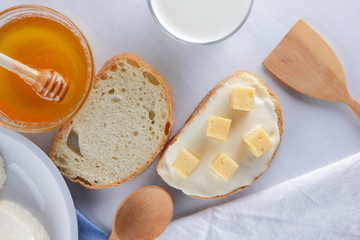 Cheese on a white plate, a glass of yogurt, a sandwich with soft cheese, minimalism, top view, copy space, a piece of bread with hard cheese, blue cloth, French breakfast, white cheese on a white back