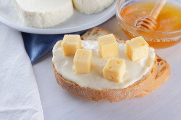 Cheese on a white plate, a glass of yogurt, a sandwich with soft cheese, minimalism, top view, copy space, a piece of bread with hard cheese, blue cloth, French breakfast, white cheese on a white back