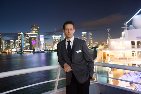 Man steward on ship board at night in miami, usa. Macho in suit jacket on city skyline. Water transport, transportation. Travelling for business. Wanderlust, adventure, discovery, journey