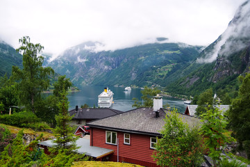 Fototapeta na wymiar Geiranger, Norway - January 25, 2010: adventure, discovery, journey. Ship in norwegian fjord on cloudy sky. Ocean liner in village harbor. Travel destination, tourism. Vacation, trip, wanderlust.