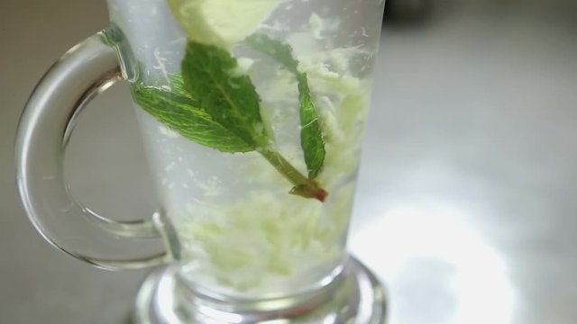 spoon stirring his tea with mint and lemon in a transparent glass, shot close-up