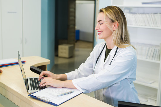 Smiling Nurse With Laptop Scheduling Appointment For Male Patient At Reception