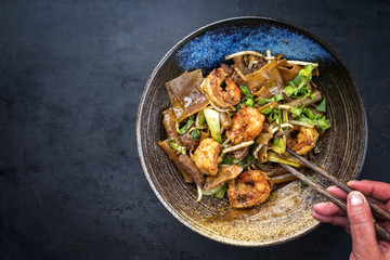 Thai Pad See Ew Noodles with vegetable and king prawns and beef as closeup in a bowl with copy space left