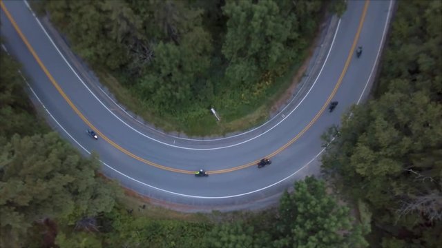 motorcycle go around tight bend in road aerial pan up to show scenic forest mountains