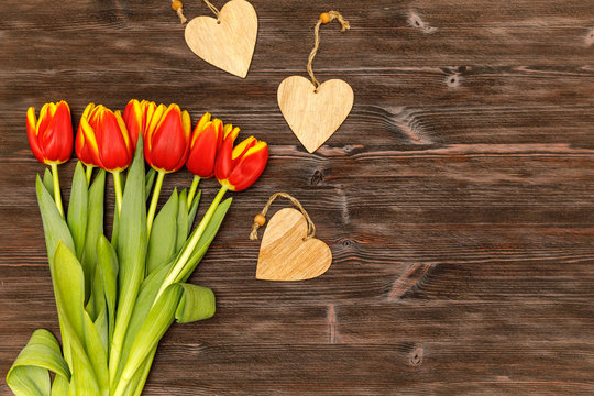 Red flowers tulips and wooden heart tags on the dark wood background, spring flatlay for mother's day