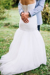 close-up of the groom's hand in a blue suit who hugs the bride in a white dress in the park