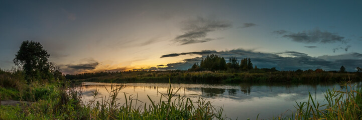 Fototapeta na wymiar evening landscape. panoramic view of the sunset from the coast of a narrow river overgrown with reeds