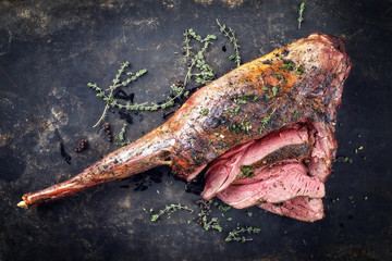 Marinated barbecue aged leg of venison sliced with herbs as top view on a rustic board with copy...
