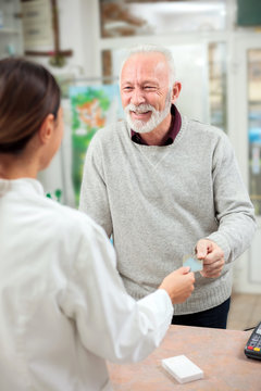 Medicine, pharmaceutics, health care and people concept - Happy senior male customer paying for medications at a drugstore