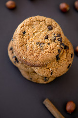 top view of cookies with chocolate around which lie nuts and cinnamon on a dark brown background