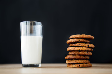 close-up of a cookie with chocolate and a glass of milk on a wooden table on a black background