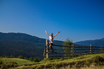 Woman with hands up on top of mountains with blue sky. Woman enjoying free happiness in beautiful landscape. Travel concept
