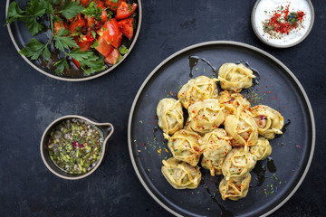 Traditional Kazakh manti steamed with mincemeat and tomato salad as top view on a modern style plate