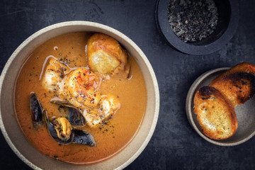 Traditional French fish soup with prawns and mussels as top view in a bowl