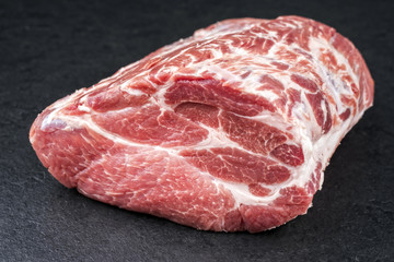 Rohes Stück Halsgrat vom Schwein angeboten offered als close-up auf einem schwarzen Board