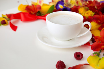 in the foreground of a white forfor-a-cup with a cup of coffee around which lie tulips, narcissus, and orchid with a red bow and raspberries on a white background