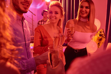 Portrait of beautiful young woman chatting with friends and  smiling happily while drinking champagne during house party in red light