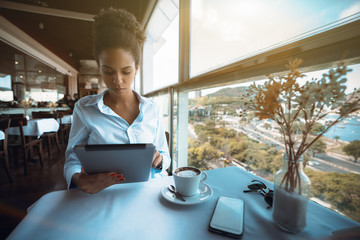 Young elegant African American girl freelancer is using a digital tablet while sitting in a luxury...