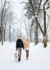 Fototapeta na wymiar Glamorous couple walking with dog in snowy park