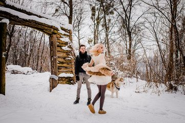 A funny couple dancing in a snowy park near their a dog
