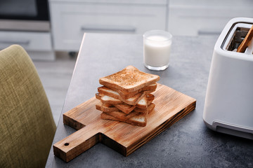 Wooden board with toasted bread and glass of milk on table