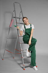 Young female decorator with paint roller on color background