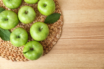 Wicker mat with fresh green apples on wooden background, top view