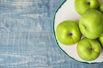 Plate with fresh green apples on wooden background, top view