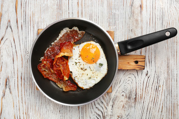 Frying pan with fried egg and bacon on wooden background