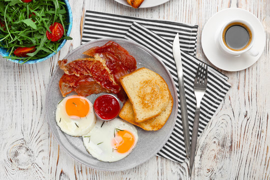 Plate with fried eggs, bacon, toasts and sauce on wooden background
