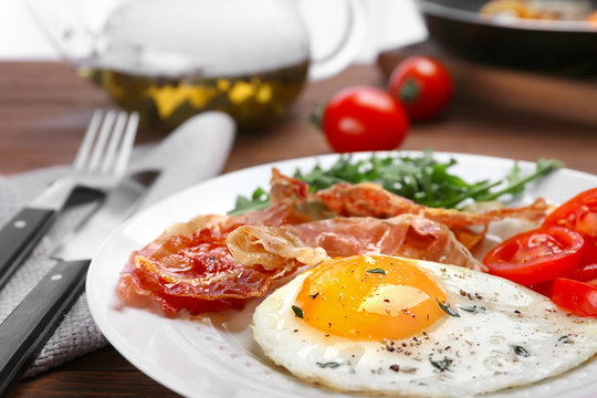 Plate with fried egg, bacon and tomatoes on table, closeup