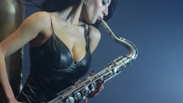 Young, beautiful, sexy, brunette woman dancing and playing golden saxophone on dark background . Shot on RED HELIUM Cinema Camera in slow motion. 