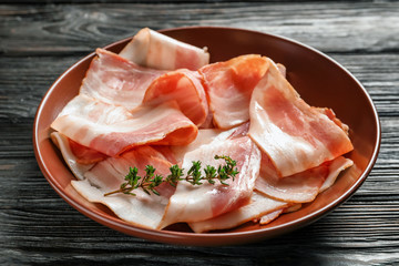 Plate with raw bacon rashers on wooden background