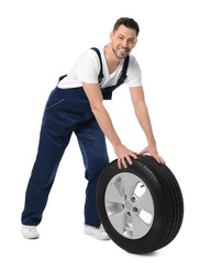 Male mechanic in uniform with car tire on white background