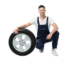 Male mechanic in uniform with car tire on white background