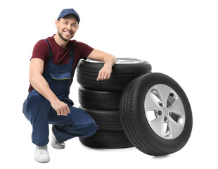 Male mechanic in uniform with car tires on white background