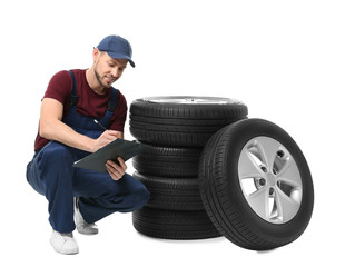 Male mechanic in uniform with car tires and clipboard on white background