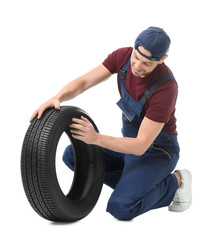 Obraz premium Male mechanic in uniform with car tire on white background