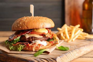 Tasty burger with bacon and french fries on wooden board