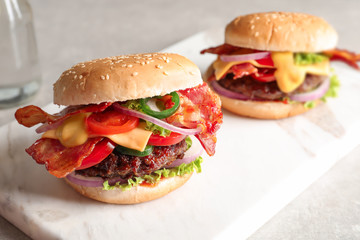 Tasty burgers with bacon on marble board
